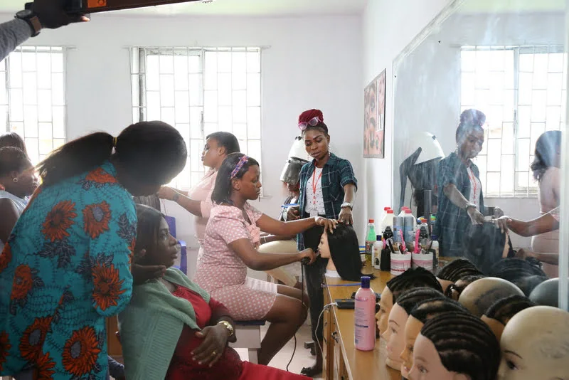 Learners practise beauty and hair techniques at benches in a mirrored classroom.