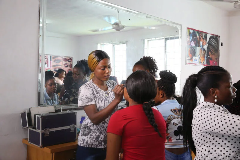 A beauty instructor demonstrates a technique while learners watch in a mirrored training room.