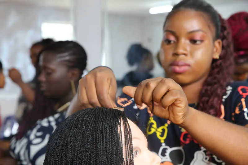 A learner carefully braids hair on a mannequin head during a practical session.
