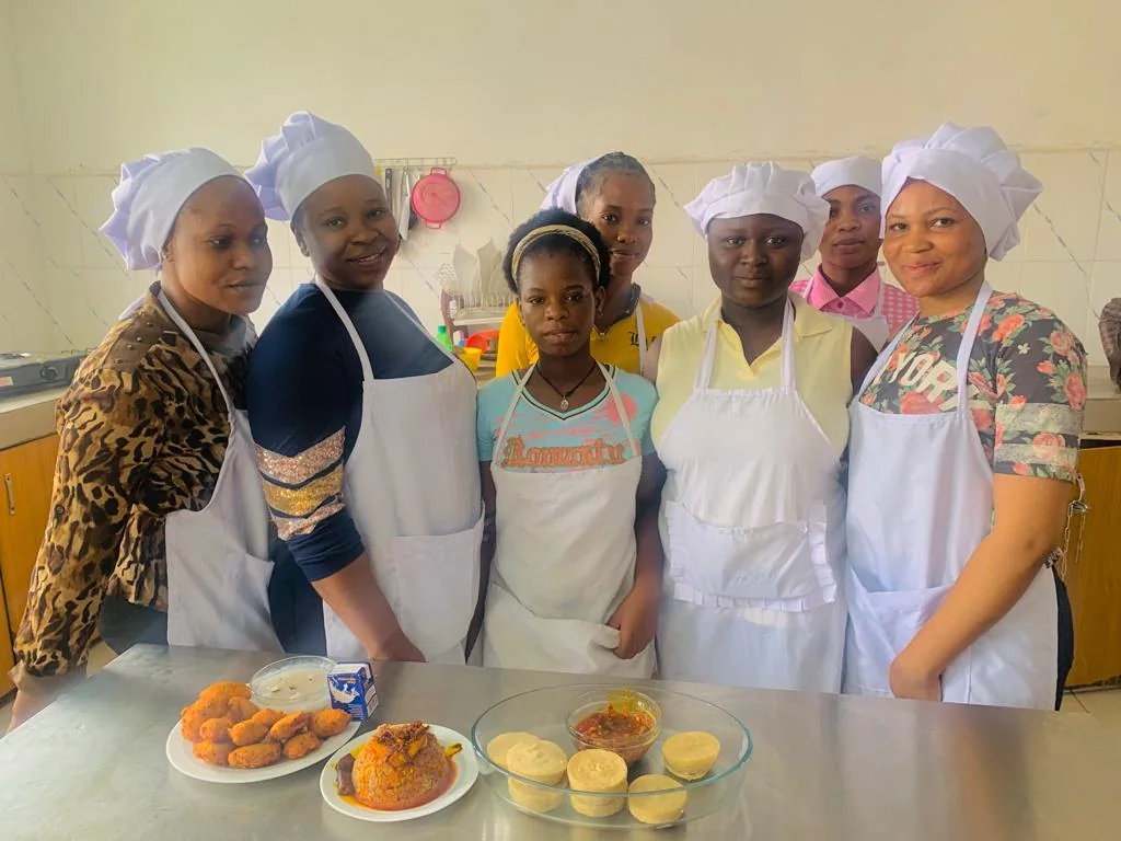 Learners in aprons and chef hats stand behind a display of prepared food.