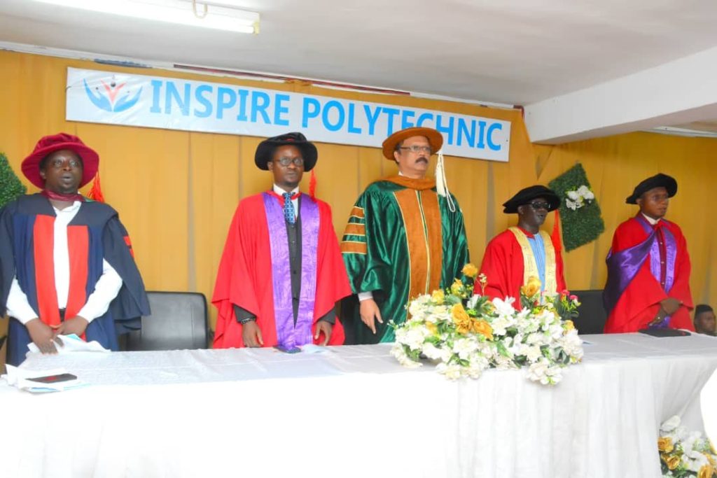 People wearing academic gowns stand behind a decorated table beneath an Inspire Polytechnic banner.