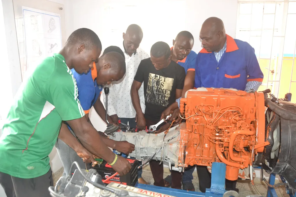 An instructor and learners work around an orange engine and transmission on a training stand.