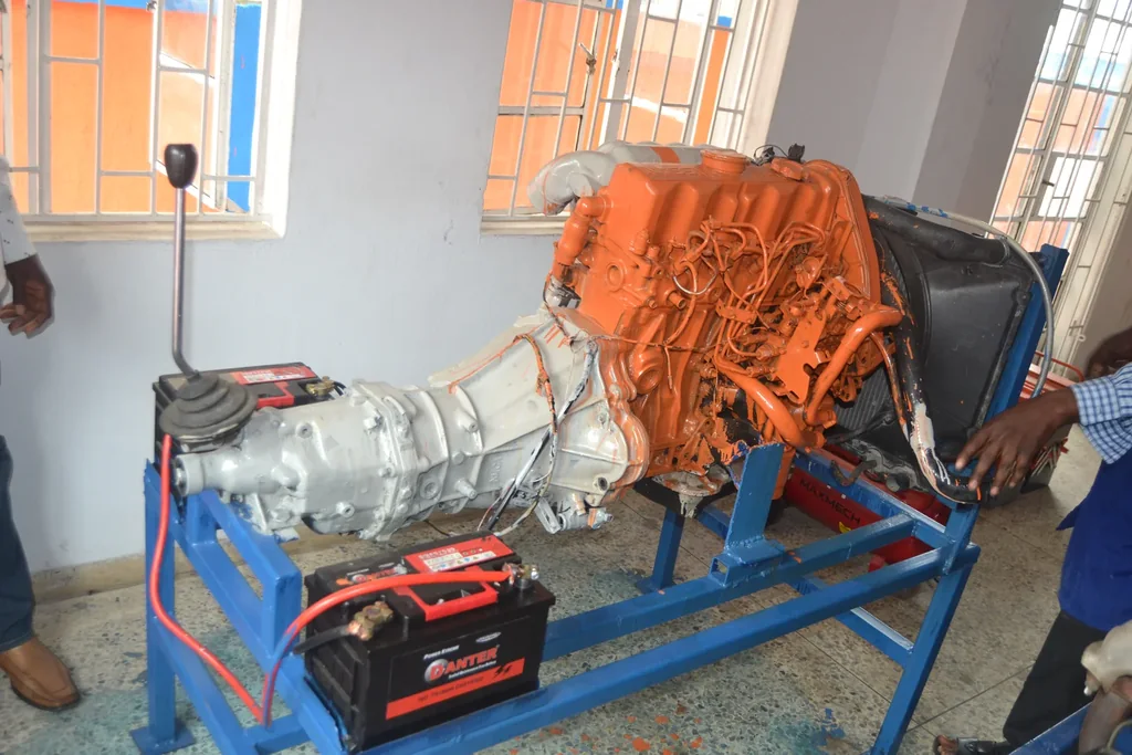 An orange engine and transmission are mounted on a blue training stand in a workshop.