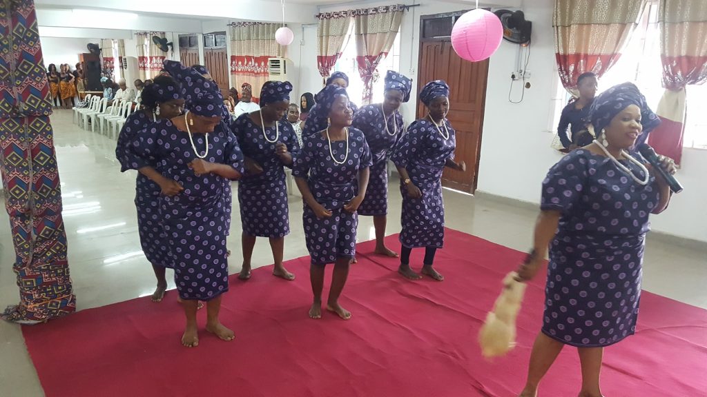 A group in coordinated patterned clothing performs on a red carpet in a decorated hall.