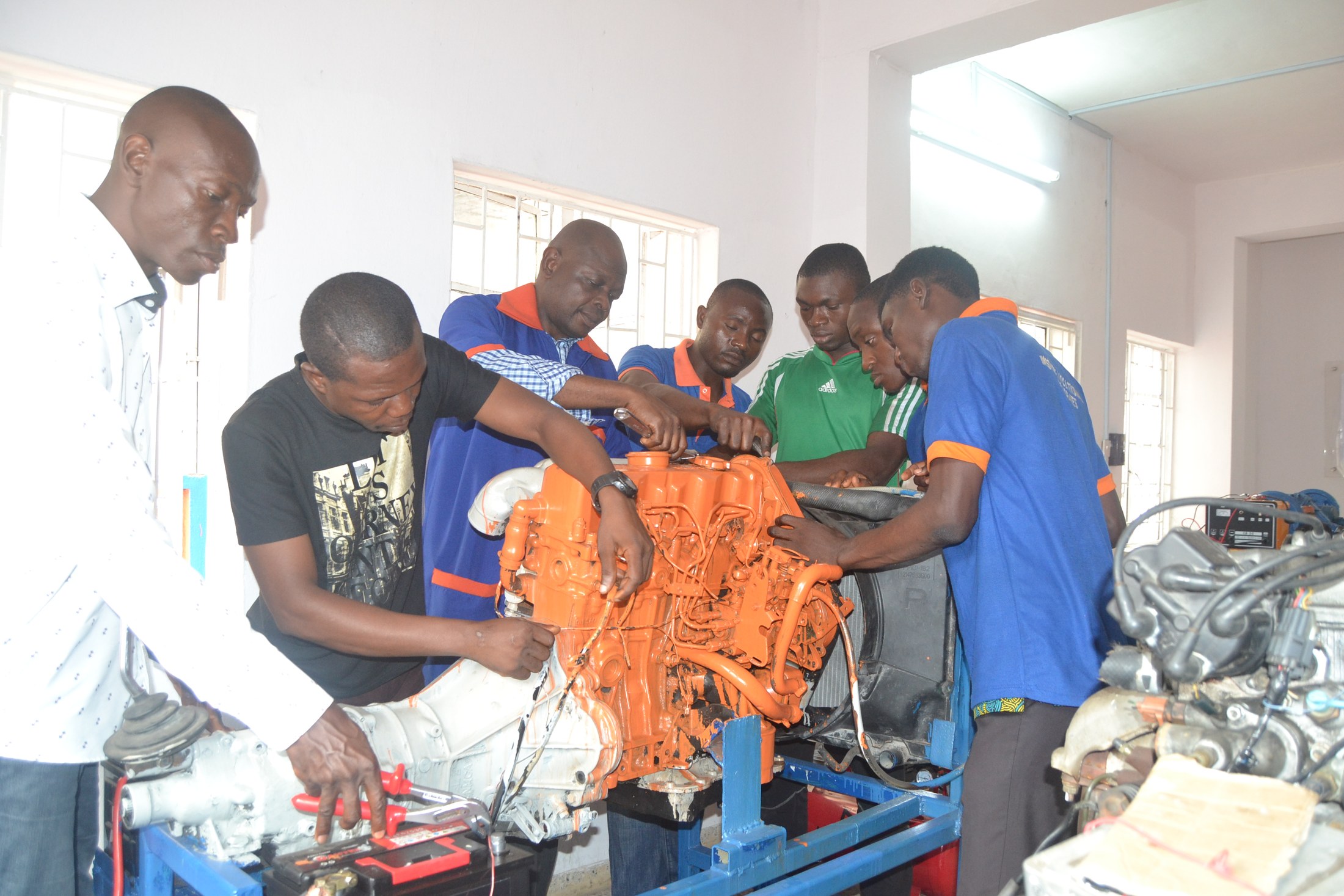 An instructor and learners gather around an engine and transmission training rig.