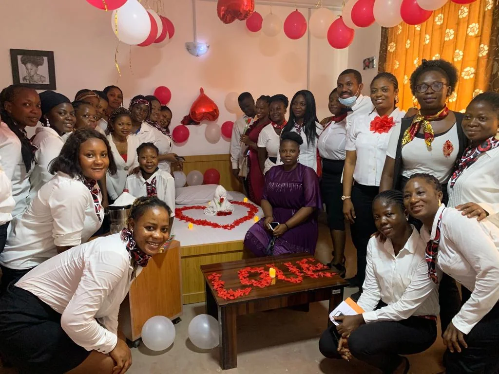 A group gathers around a cake and decorated table with red and white balloons.