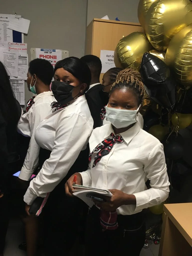 Students in white shirts and patterned neckties stand together at an indoor event.