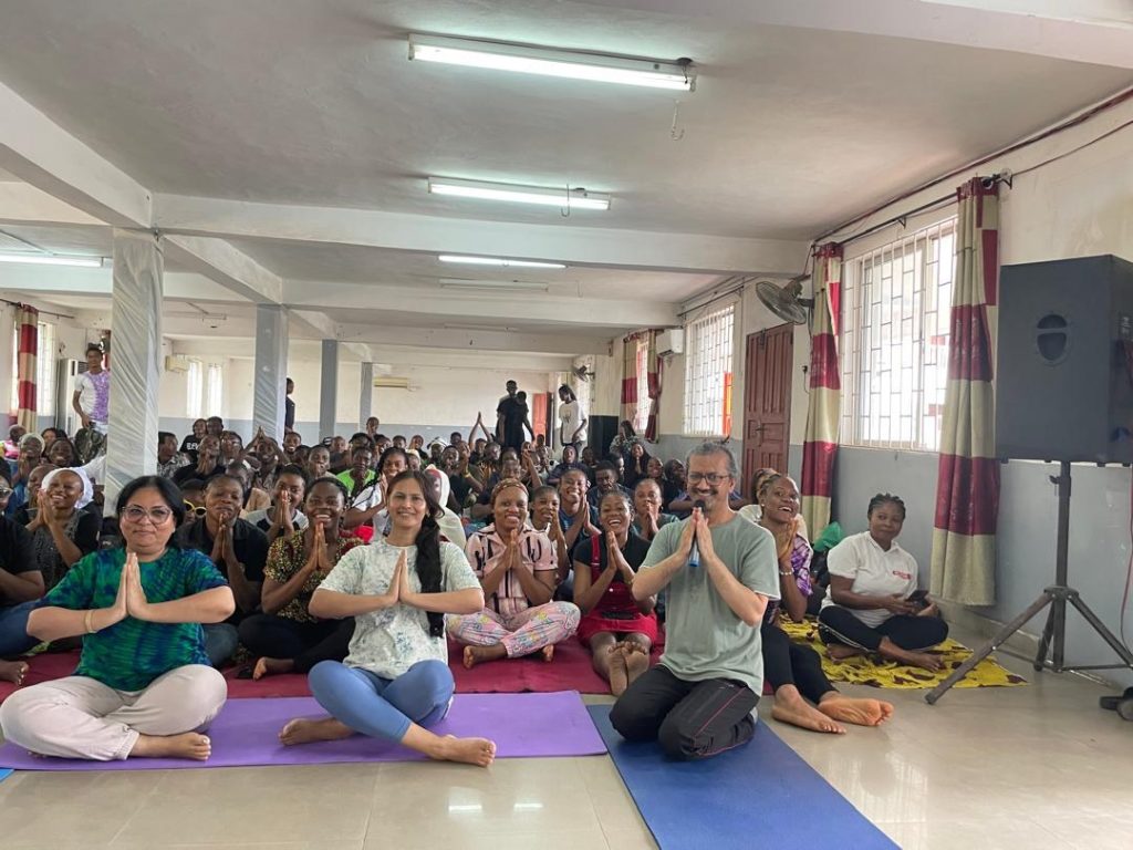 Participants sit together on mats in a hall during a wellbeing activity.