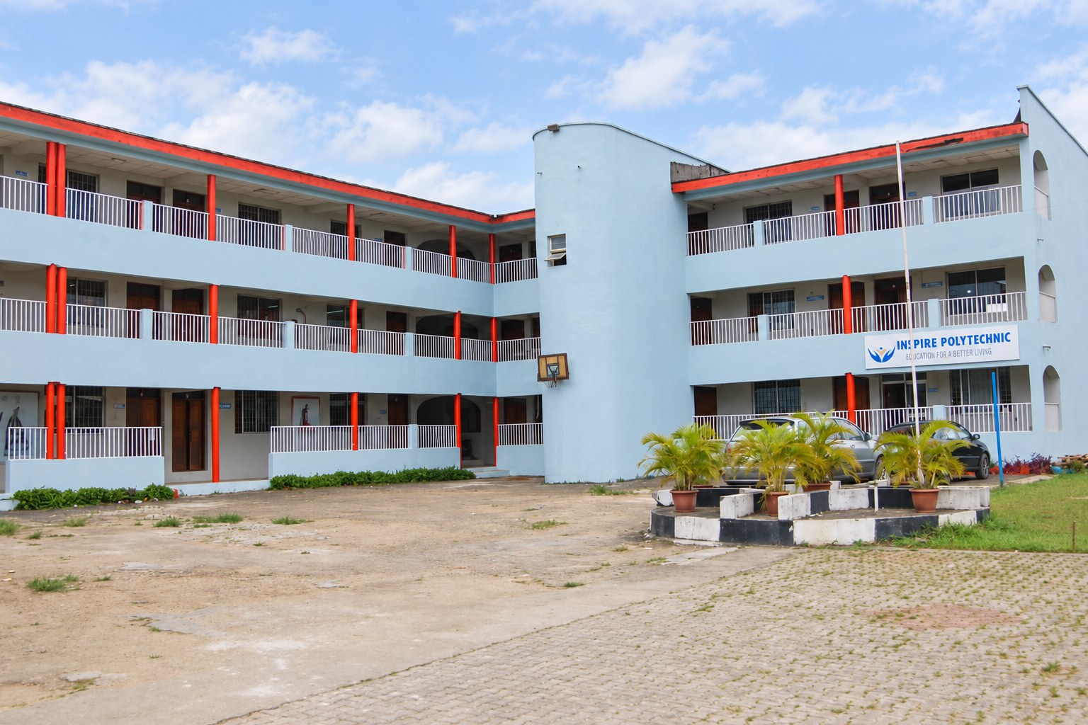 The Inspire Polytechnic courtyard, with pale blue teaching blocks, red columns and palm planters.
