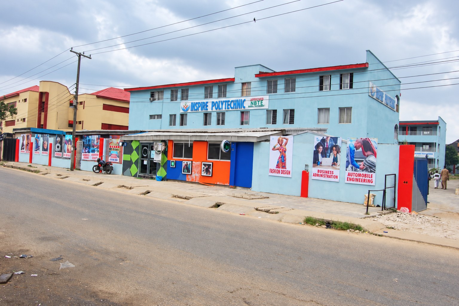 Street view of the Inspire Polytechnic entrance, pale blue college building and colourful course displays.
